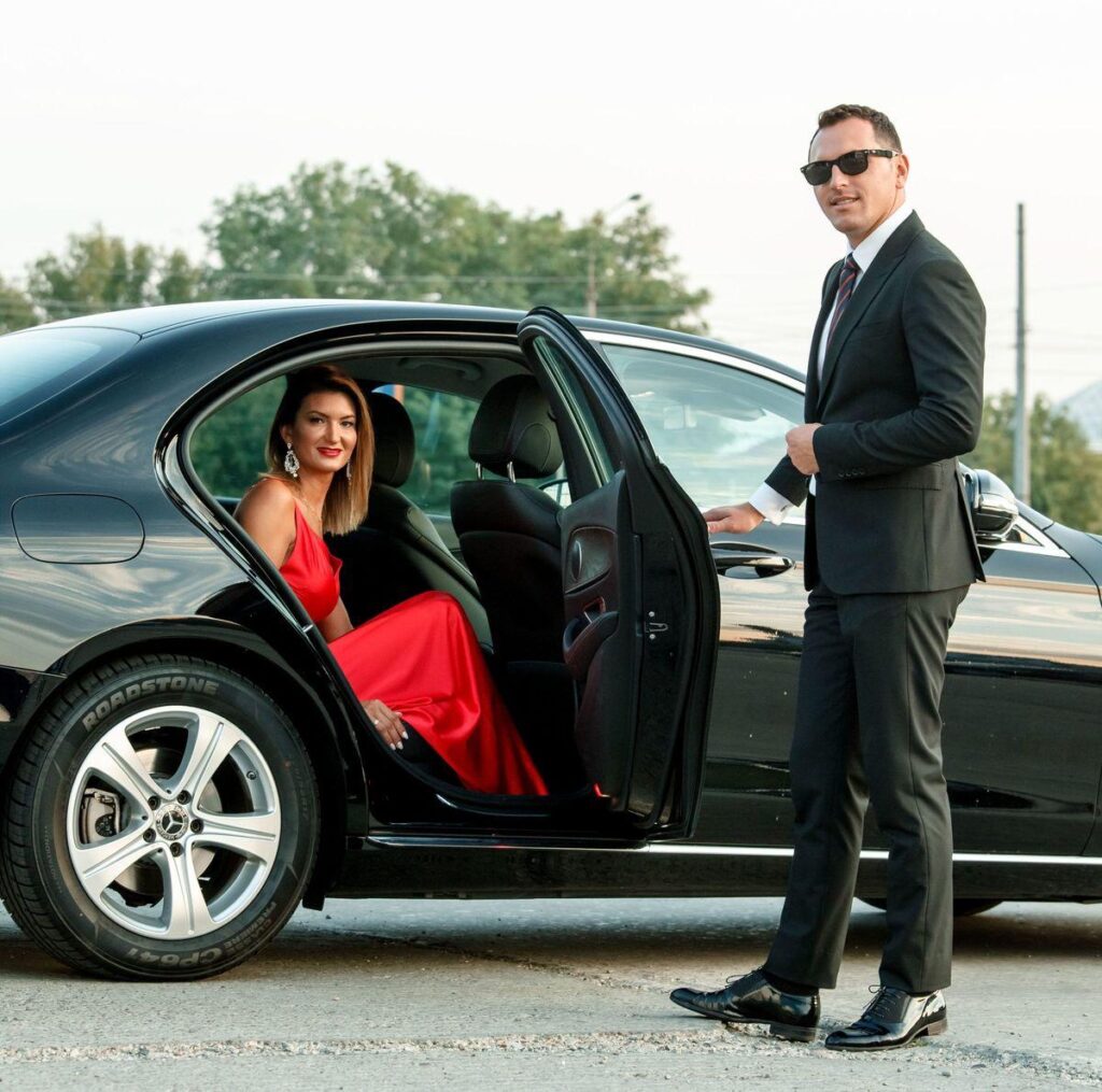 A man and woman in formal wear sitting inside of a car.