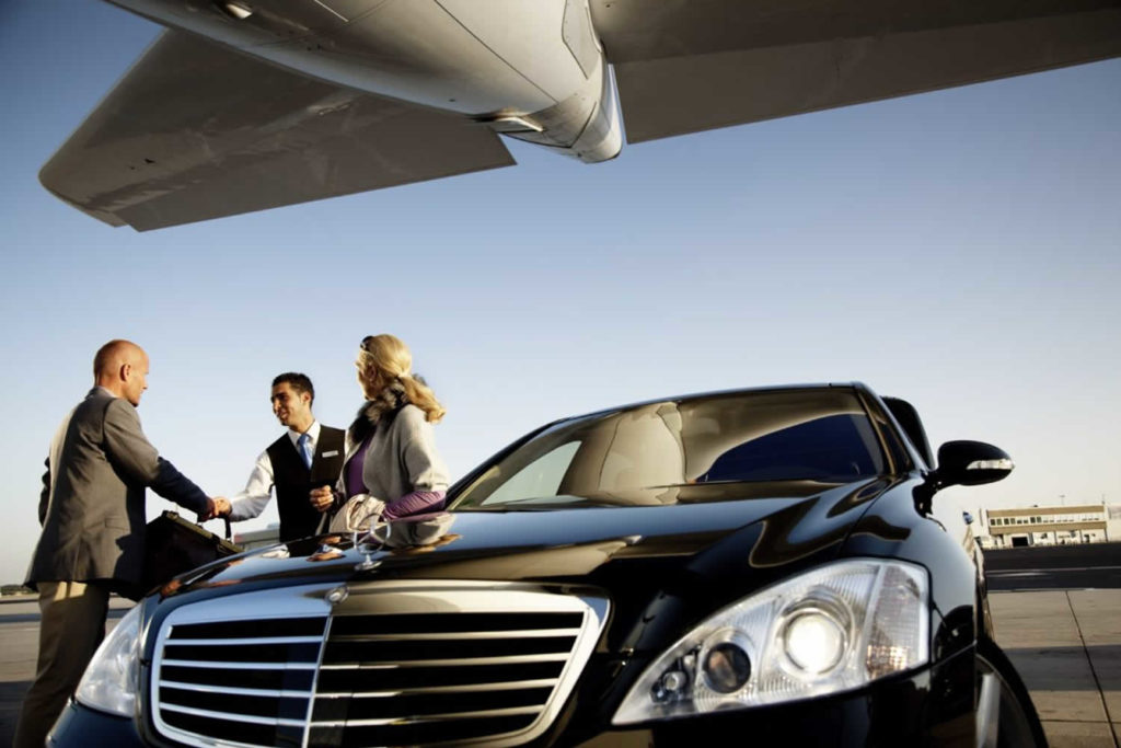 A man and woman standing next to a black car.